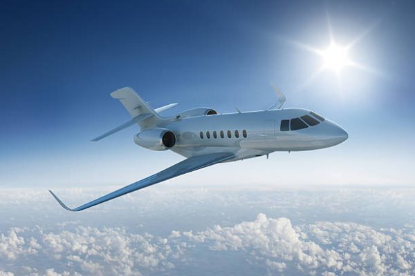Private jet flies past sun - in blue sky above the clouds